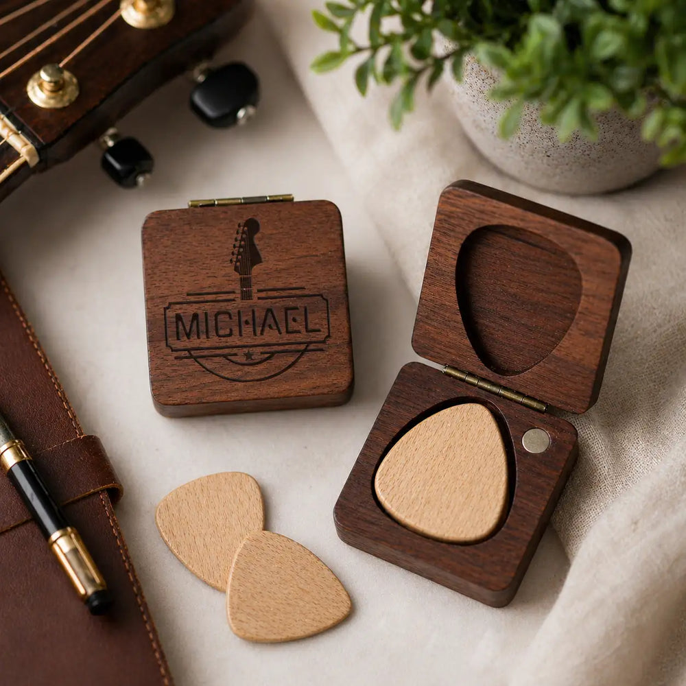 Dark wood guitar pick case with engraved name and logo, containing a light-colored wooden pick.