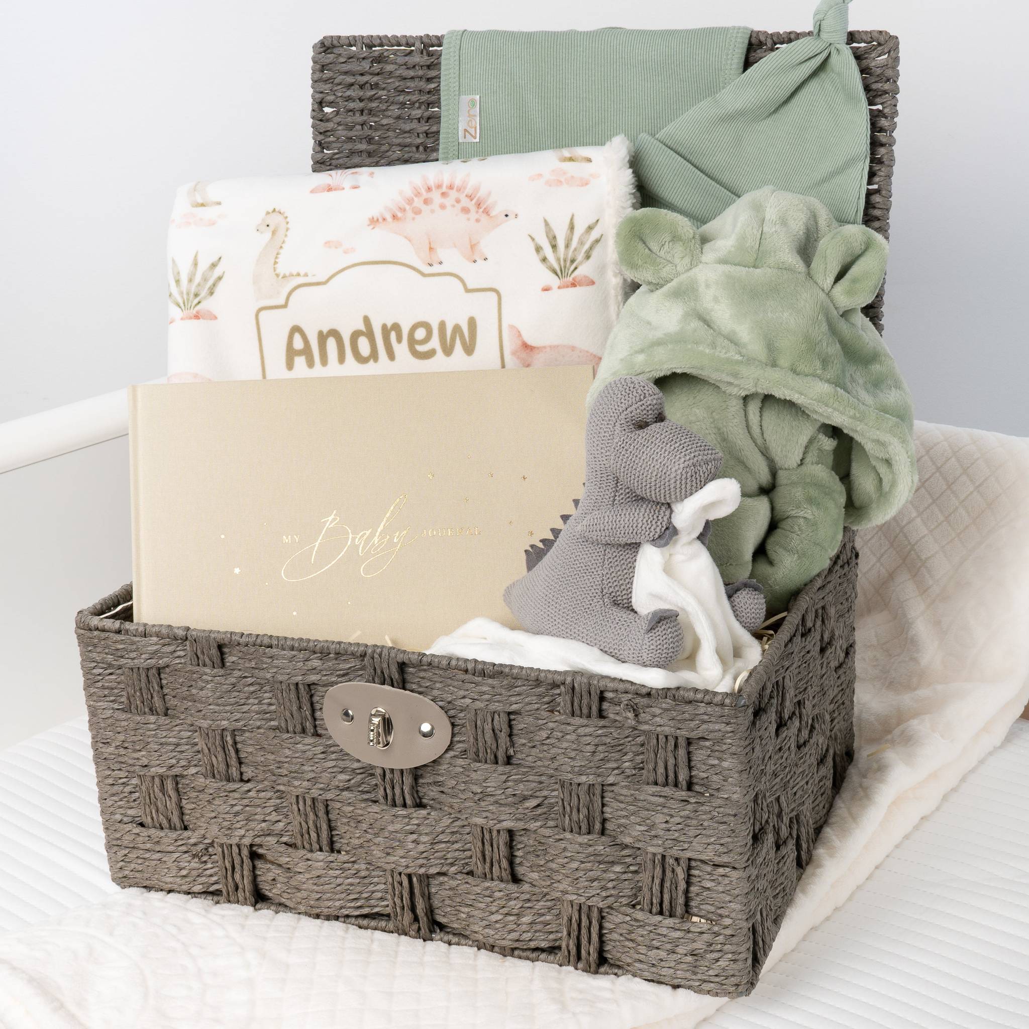 Woven basket with baby items including a blanket, toy, and card on a white surface. Main image
