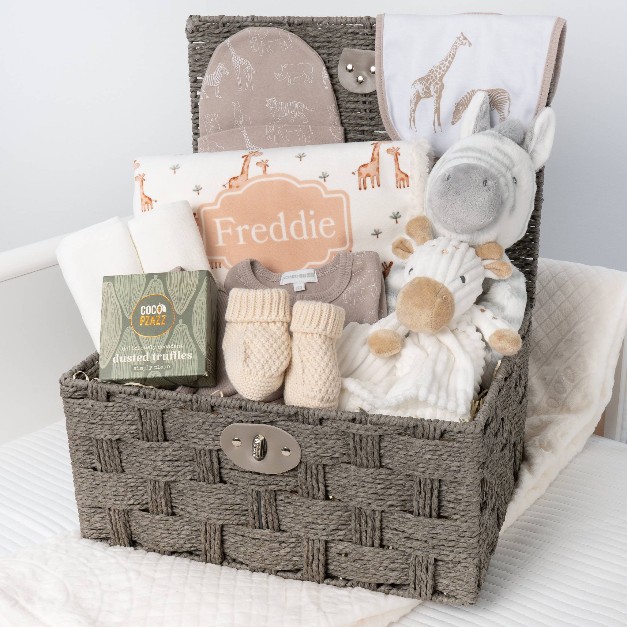 Baby gift basket with plush toys, clothing, and baby products on a white blanket. Main image
